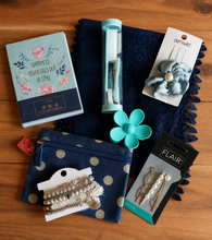 Load image into Gallery viewer, A curated flat-lay of various hair accessories and stationery items arranged on a dark blue lace scarf over a wooden table. The set includes a floral notebook, a mini manicure set, a blue fabric hair claw clip on a card, pearl hair pins on a card, and bracelets on a card.