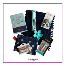 Load image into Gallery viewer, A curated gift set of hair accessories and stationery items arranged on a white background with a decorative border. The set includes a navy blue pouch with polka dots, a turquoise flower-shaped hair clip, a mini manicure sets, a floral hair accessory, bracelets, and a small notebook.