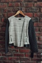 Load image into Gallery viewer, Jacket hanging on a wooden hanger against a brick wall.