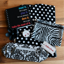 Load image into Gallery viewer, A flat-lay collection of black and white patterned fabric accessories on a wooden surface, including a black polka dot snoodk, a zebra-print zip pouch, a damask-patterned cosmetic bag, a black flower-shaped hair clip and a small round tin with lip balm.