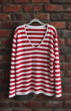 Load image into Gallery viewer, A red and white horizontally striped long-sleeve V-neck top hanging on a gray hanger against a red brick wall.