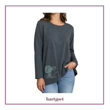 Load image into Gallery viewer, A woman wearing a dark gray long-sleeve top with a white graphic print near the lower left hem, paired with light blue jeans. The brand name 'hartgoet' is printed below the model on a white background with a thin purple border.
