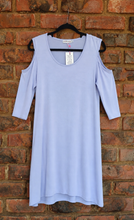 Load image into Gallery viewer, A lilac cold-shoulder tunic top with three-quarter sleeves, hanging on a black hanger against a red-brown brick wall.