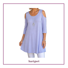 Load image into Gallery viewer, A woman wearing a light lavender cold-shoulder tunic top with three-quarter sleeves, paired with white leggings. The image is framed with a purple border and features the brand name 'hartgoet' at the bottom.