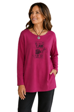 Load image into Gallery viewer, A woman wearing a bright cerise pink long-sleeve tunic top with a vintage-style graphic print on the front, paired with black pants, standing against a white background.