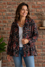 Load image into Gallery viewer, A woman wearing a long-sleeve button-up shirt jacket with a dark red, black, and white paisley pattern, styled over a white tank top and blue jeans, standing in front of a red brick wall.