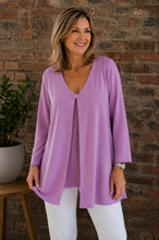 Load image into Gallery viewer, A woman wearing a lavender purple long-sleeve open front jacket with one button, and white pants, standing in front of a rustic brick wall.