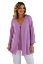 Load image into Gallery viewer, A woman wearing a lavender purple long-sleeve tunic top with a V-neck and white pants, standing against a white background.