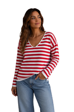 Load image into Gallery viewer, A woman wearing a red and white horizontally striped long-sleeve V-neck top with light blue jeans, standing against a white background.
