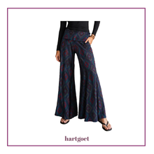 Load image into Gallery viewer, A model is shown from the waist down wearing a pair of wide-leg pants with a dark navy blue base and a red and blue geometric diamond pattern. The model is also wearing a black long-sleeve top and black sandals.