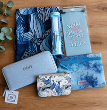 Load image into Gallery viewer, A flat-lay collection of blue-themed gift items on a wooden tabletop, including a blue patterned scarf, a mini manicure set, a light blue textured wallet with gold 'ESCAPE' lettering, a small card wallet, a light blue magnetic notepad with motivational text, and a coin purse.