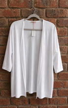 Load image into Gallery viewer, A white open-front lightweight jacket with three-quarter sleeves hanging on a gray hanger against a red-brown brick wall.