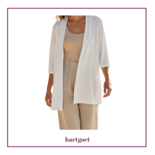 Load image into Gallery viewer, A woman wearing a white open-front cardigan over a beige tank top and beige pants, shown against a white background with a thin purple border and the brand name hartgoet below.
