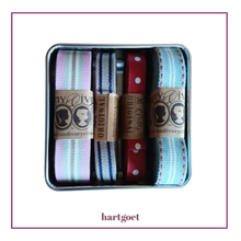 Load image into Gallery viewer, A square metal gift tin containing four decorative ribbons in pastel and solid colors, each wrapped with a paper band. The bands show the hartgoet brand name and logo.
