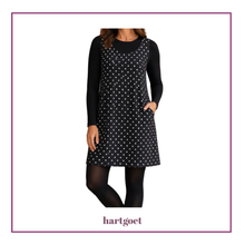 Load image into Gallery viewer, A woman wearing a black sleeveless dress with a white polkadot pattern over a black long-sleeve top, paired with black tights. The brand name 'hartgoet' is printed below the image.
