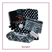 Load image into Gallery viewer, A coordinated black-and-white patterned stationery and accessory set on a white background with a thin purple border. The set includes a spiral notebook with colorful motivational text, a black-and-white polka snood, a zebra-print zip pouch, a black-and-white damask pouch, a small round tin with lip balm, and a flower hair clip.
