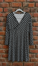 Load image into Gallery viewer, Black and white polkadot dress on a hanger against a brick wall

