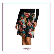 Load image into Gallery viewer, A model wearing a black skirt with a vibrant multicolor floral print, paired with a black long-sleeve top. The brand name 'hartgoet' is printed below the model on a white background with a thin purple border.
