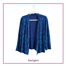 Load image into Gallery viewer, A blue open-front cardigan with a teal floral pattern, hanging on a white hanger against a white background with a purple border. The brand name 'hartgoet' is printed below.
