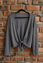 Load image into Gallery viewer, Charcoal bolero cardi on a hanger against a brick wall
