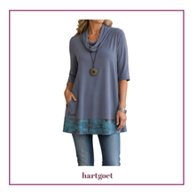 Load image into Gallery viewer, A woman wearing a cowl-neck tunic top in grey with a teal patterned hem, paired with blue jeans, shown against a white background with a purple border.
