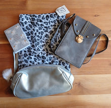 Load image into Gallery viewer, A flat-lay of a small notebook, a black and white leopard-print scarf, a gray suede crossbody with gold hardware, and a metallic silver zippered bag with a white pom-pom charm.
