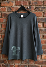 Load image into Gallery viewer, A dark gray long-sleeve t-shirt with a white line art graphic of a windmill on the lower left front, hanging on a black hanger against a red brick wall.
