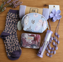 Load image into Gallery viewer, A flat-lay arrangement of beauty accessories on a wooden surface, including patterned socks, a lavender flower-shaped hair clip, a purple beaded necklace, a tube of nail care tools, a small floral card wallet, a lilac scarf and a small cosmetic bag with butterfly print. 
