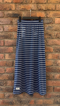 Load image into Gallery viewer, A navy blue and white horizontally striped midi skirt hanging from a black hanger against a red-brown brick wall.
