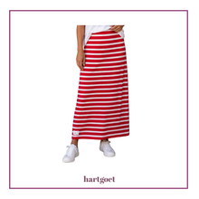 Load image into Gallery viewer, A model wearing a red and white horizontally striped maxi skirt with a white t-shirt and white sneakers, shown against a white background with a purple border and the brand name 'hartgoet' at the bottom.
