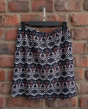 Load image into Gallery viewer, Aztec print mini skirt on a hanger against a brick wall 
