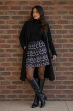 Load image into Gallery viewer, Model wearing an aztec print mini skirt, black top and jacket and black boots, standing against a brick wall

