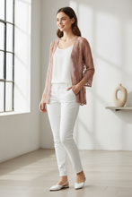 Load image into Gallery viewer, A woman stands in a bright, sunlit room wearing a white tank top, white pants, white flats, and a sheer blush brown lace cardigan.
