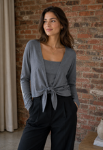 Load image into Gallery viewer, Model wearing a charcoal bolero cardi and black pants and standing against a brick wall.
