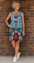 Load image into Gallery viewer, Woman wearing a colourful mandala print dress, standing against a brick wall
