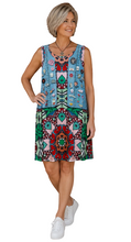 Load image into Gallery viewer, A woman with short blonde hair stands against a white background, wearing a sleeveless, knee-length dress with a colorful bohemian mandala pattern in blue, green, red, and pink, paired with white sneakers.
