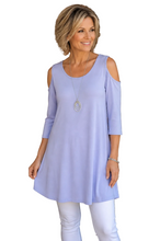 Load image into Gallery viewer, A woman wearing a light lavender cold-shoulder tunic top and white pants, standing against a white background.  
