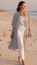 Load image into Gallery viewer, Woman walking on a sandy beach wearing a long white and charcoal striped jacket and white pants.
