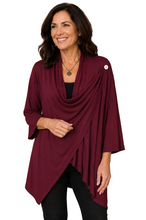 Load image into Gallery viewer, A woman wearing a draped burgundy wrap top over a black top and black pants, standing against a white background.
