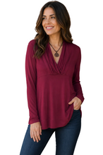 Load image into Gallery viewer, A woman wearing a long-sleeve burgundy wrap-style top and dark blue jeans, standing against a white background.
