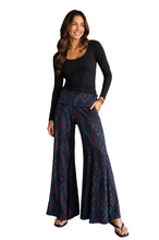 Load image into Gallery viewer, A woman modeling a black long-sleeve scoop-neck top and high-waisted, wide-leg pants featuring a dark blue and burgundy geometric pattern, paired with black flip-flop sandals against a white  background.
