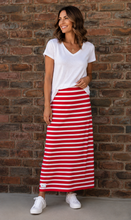Load image into Gallery viewer, A woman stands against a brick wall wearing a white V-neck short-sleeve t-shirt and a red and white horizontally striped maxi skirt, paired with white sneakers.

