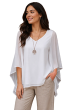 Load image into Gallery viewer, A woman wearing a white V-neck blouse with wide, draped batwing sleeves and light beige pants, standing against a white background.
