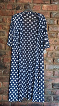 Load image into Gallery viewer, A navy blue open-front long jacket with white polka dots, hanging on a dark hanger against a red-brown brick wall.
