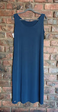 Load image into Gallery viewer, A sleeveless navye blue long sleeveless dress hanging on a gray hanger against a red brick wall background.
