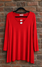 Load image into Gallery viewer, A bright red long-sleeve V-neck tunic top hanging on a black hanger against a rustic brick wall background.
