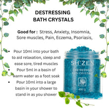 Load image into Gallery viewer, Promotional graphic for SH'ZEN Destressing Bath Crystals, showing a clear jar filled with blue crystals on a white background with green leafy vine borders. Text lists benefits for stress, anxiety, insomnia, sore muscles, pain, eczema, and psoriasis, with usage instructions below the product photo.
