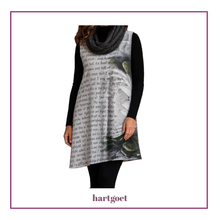 Load image into Gallery viewer, A woman wearing a sleeveless tunic dress with a black and white script and floral print, styled over a black long-sleeve top and a chunky gray knit scarf, shown against a white background with a purple border.
