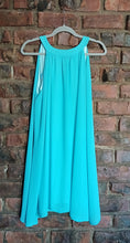 Load image into Gallery viewer, A sleeveless turquoise blue dress hanging on a gray hanger against a red-brown brick wall.
