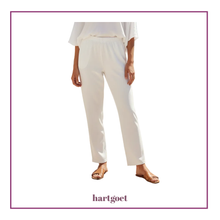 Load image into Gallery viewer, A model wearing a pair of white trousers with an elastic waistband, paired with a white top and brown flat sandals, shown against a white background with a purple border and the brand name 'hartgoet' at the bottom.
